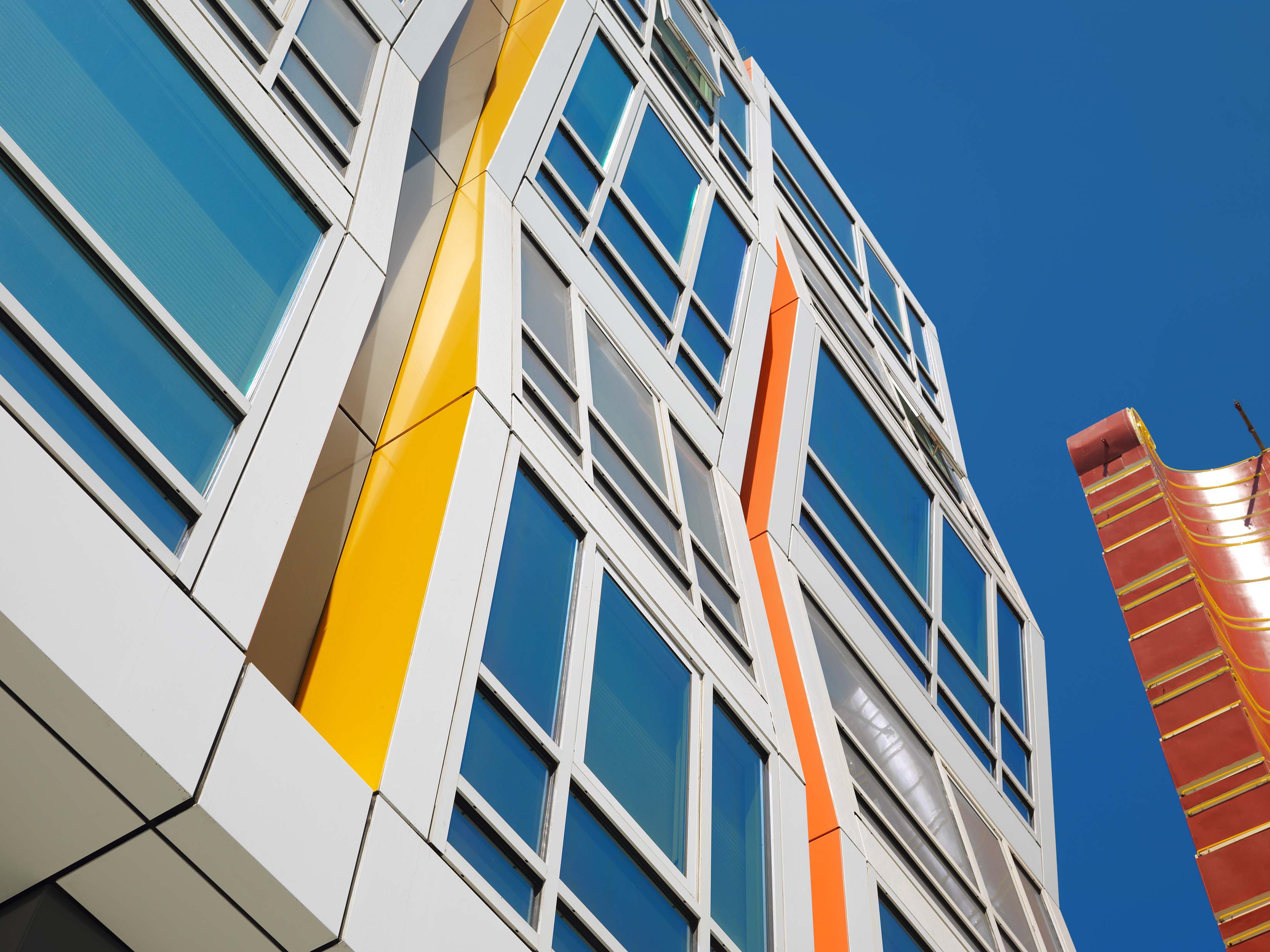 This large building has various window designs, and the building is appearing to bend in and out in a unique way. The siding is white, yellow and orange. 