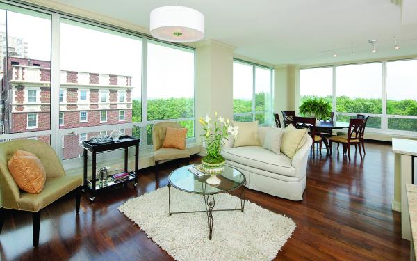 The inside of an 801 Skinker apartment. There are eight large, floor to ceiling windows with silver trim from Winco Windows, tan furniture, dark hardwood floors and a round table with chairs.
