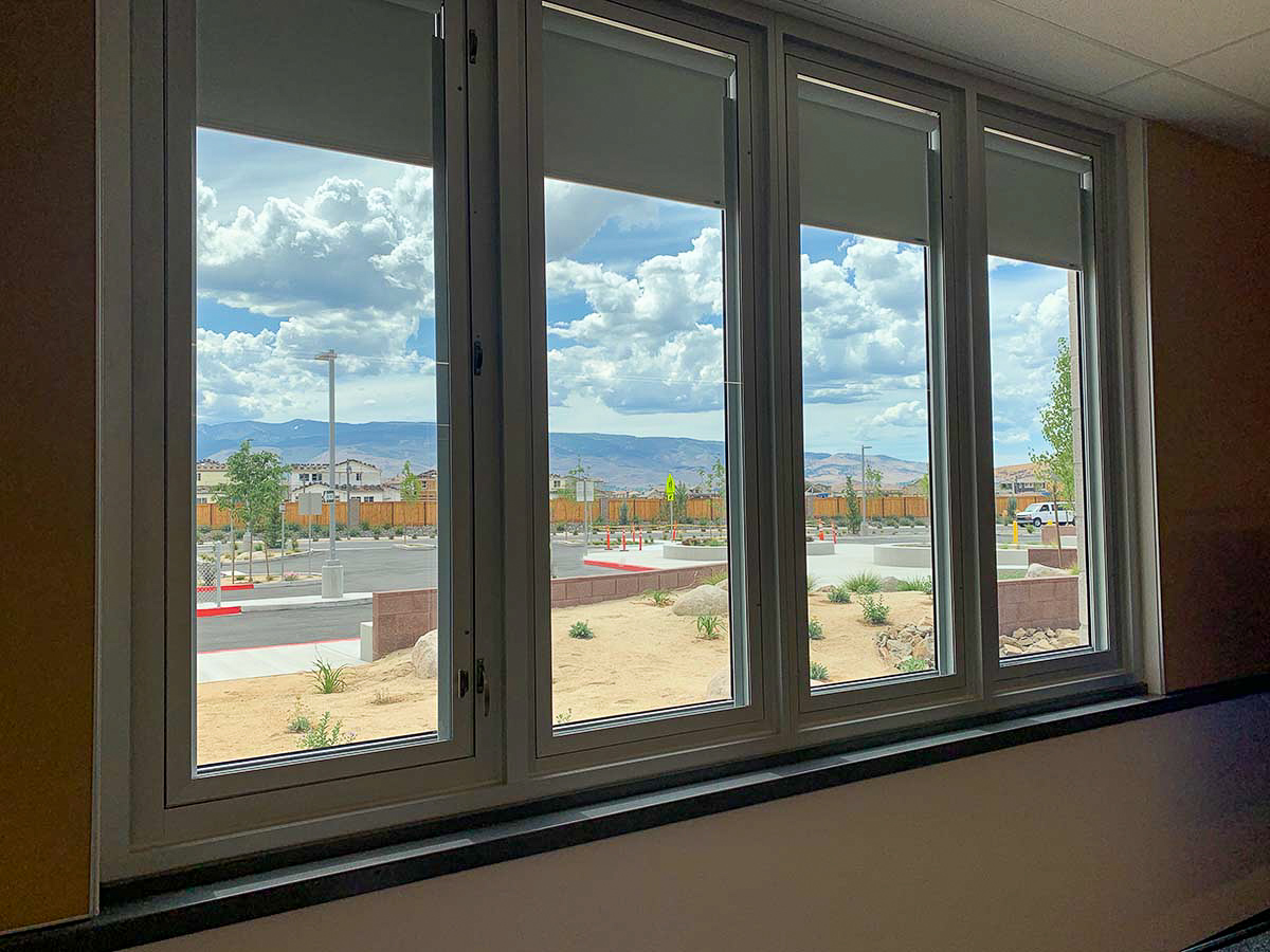 These four windows all have shades. These windows overlook a parking lot.