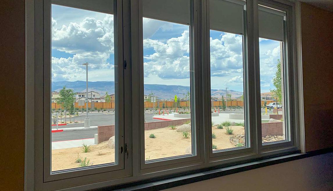 Four windows overlook a parking lot. There are mountains in the distance, and clouds cover the blue sky. 