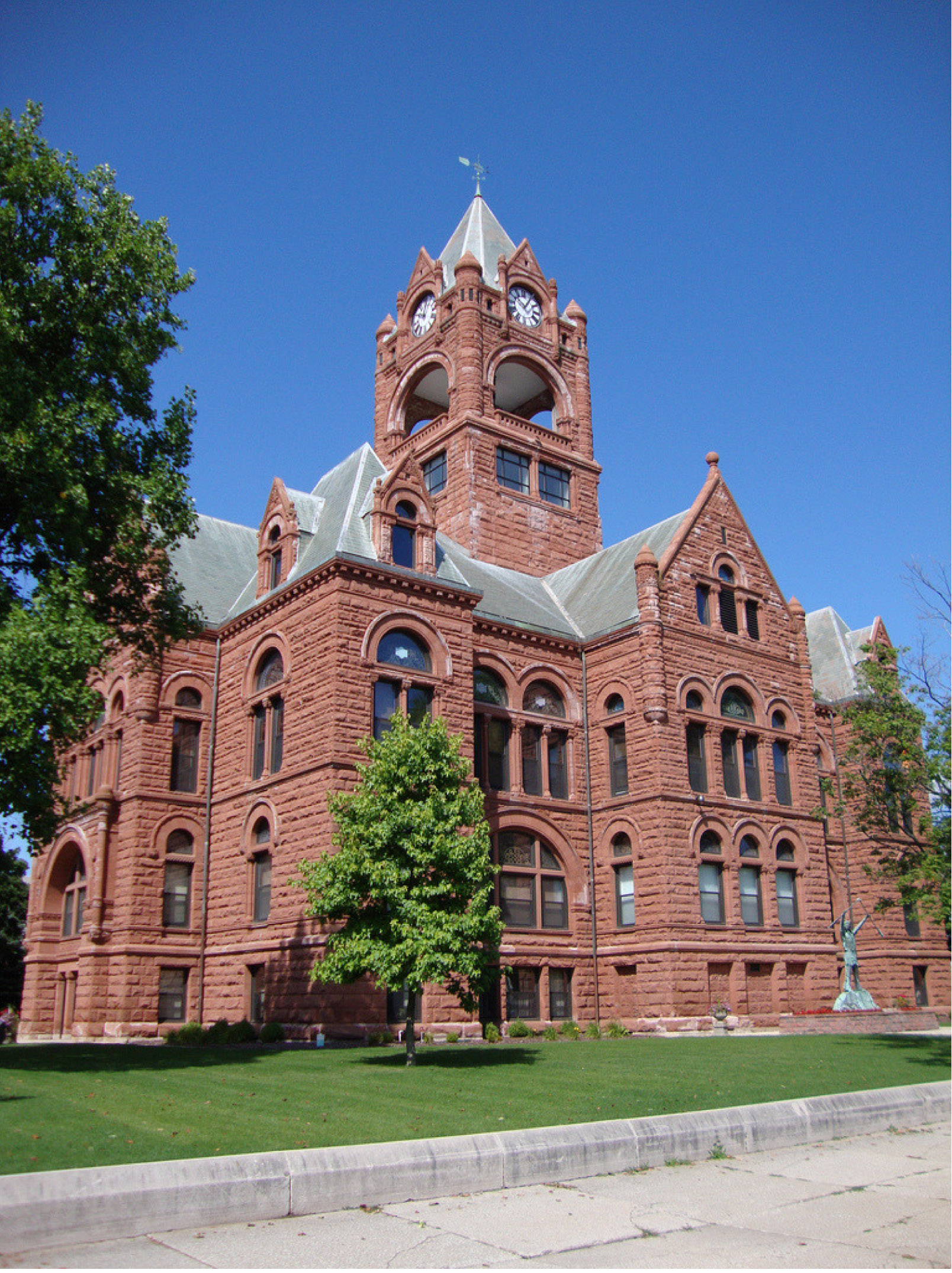 This brick courthouse building has green grass and green trees surrounding the building. 