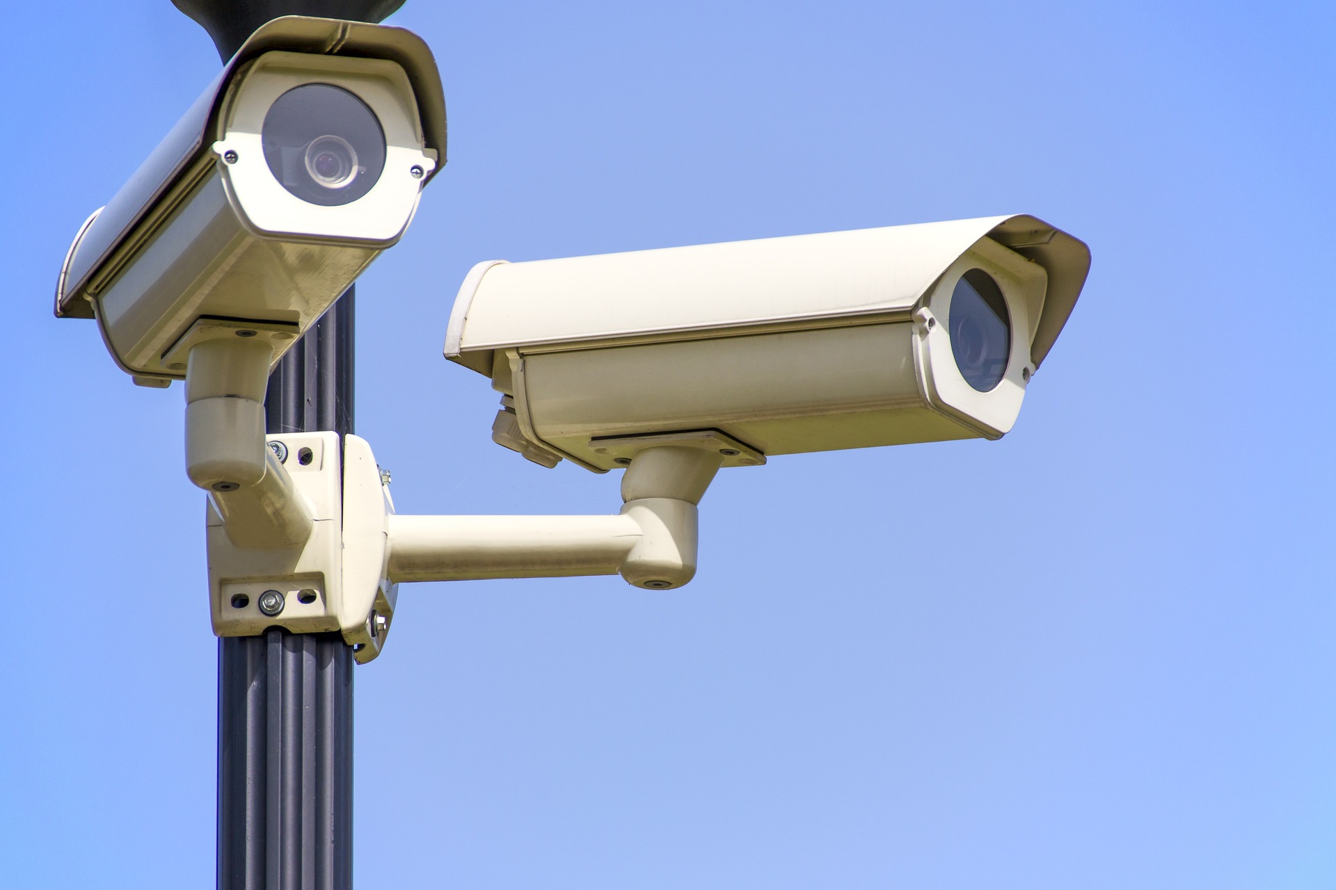 Two white security cameras pointed in different directions mounted on a black street lamp.
