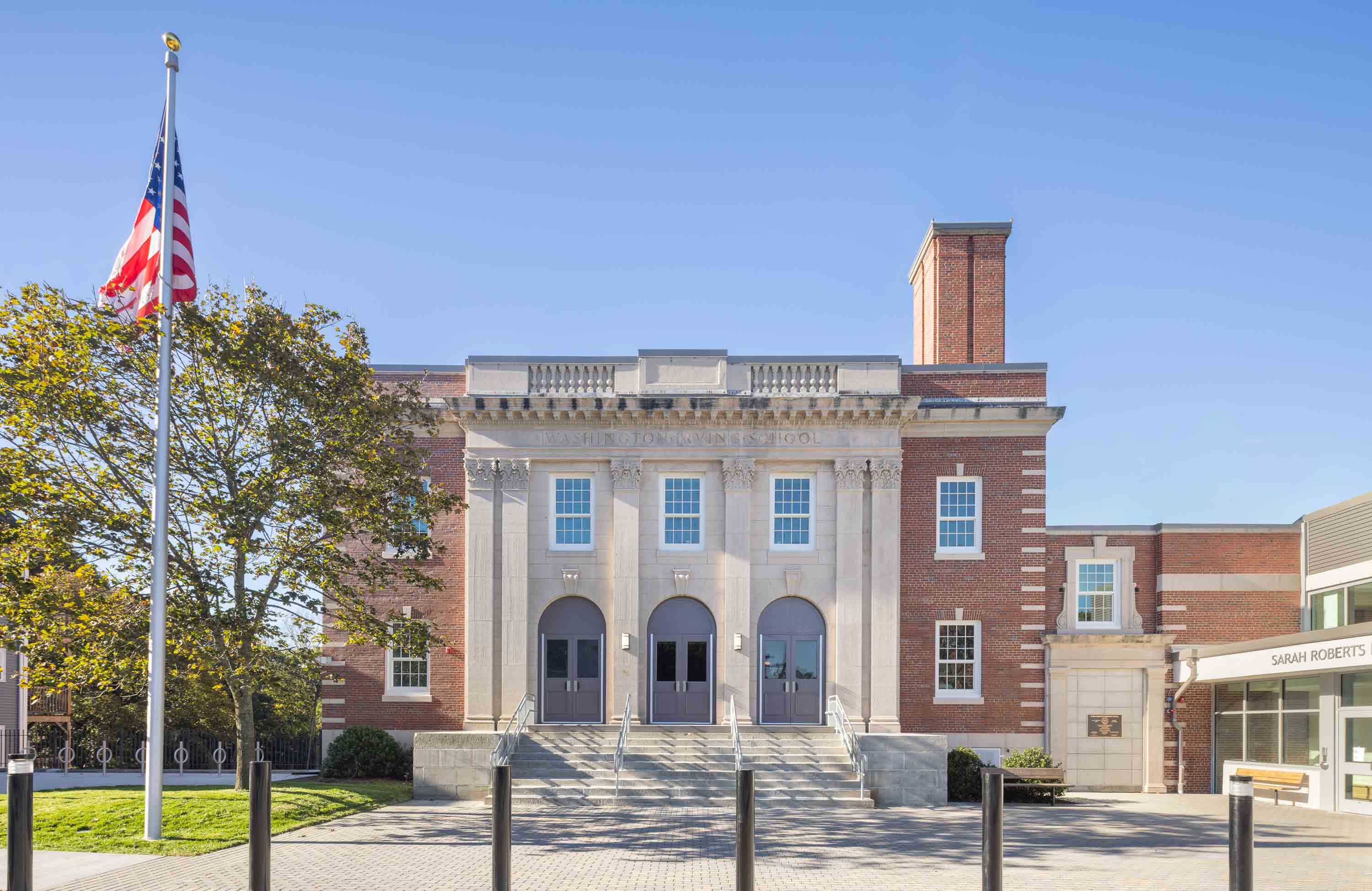Exterior brick building featuring historic replica windows with a grassy field in front and blue sky in the background.
