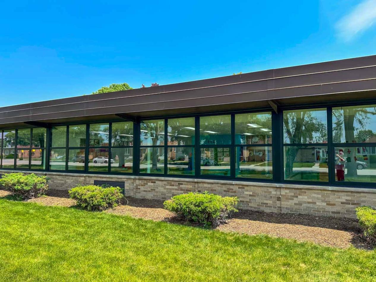 Winco's 1150 series windows' with a dark bronze anodized aluminum finish, dramatically improved the brick façade at Harry E Fry Elementary School. Building facade showcasing large dark bronze anodized windows, complemented by a grassy landscape in front.