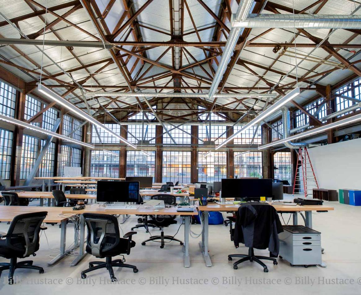 WINCO provided more than 48,000 square feet of its Series 3250 Steel Replica windows fitted with ¼” monolithic tempered clear glass. In addition to stunning aesthetics, the windows can withstand 110 mph winds as well as seismic activity. A large indoor room featuring a desk with chairs, with natural daylight illuminating the space.