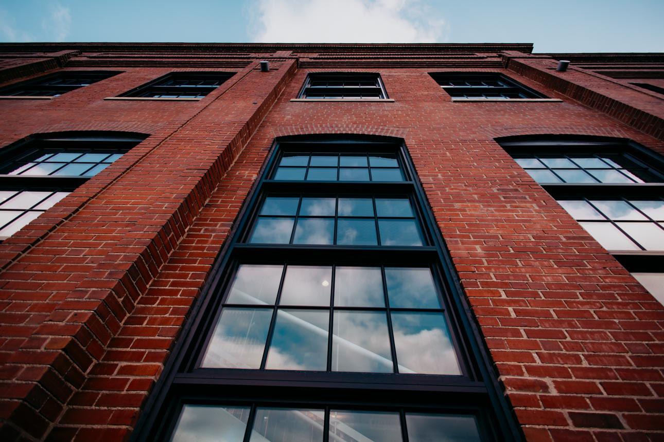Kings Hill featuring Winco's 1150S series windows finished with black Kynar paint, include a black spacer and muntins to replicate the original windows, and provide energy efficiency. Close up of brick building with large historic replica window