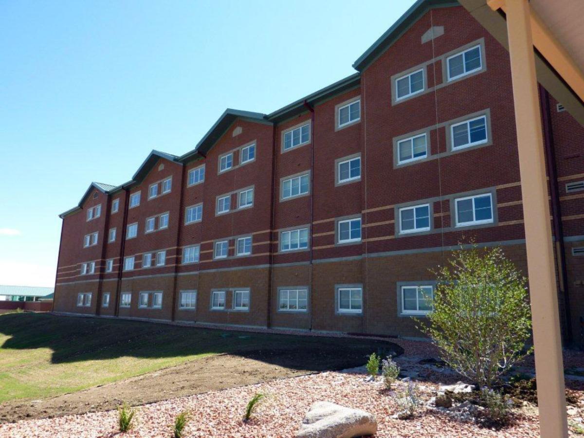 All apartments have Winco’s 3410 sliding window series installed with blast-resistant laminated glass. A large building featuring numerous sliding windows, surrounded by greenery including trees and grass, under a clear blue sky.