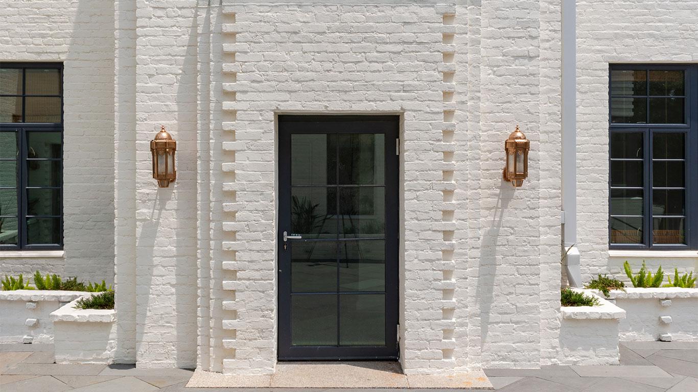 Farnsworth Apartments using Winco's Hurricane Resistant 3250 Steel Replica windows and NC-82 doors. A white brick building featuring a large door, equipped with WINCO’s NC82 Terrace Doors for hurricane resistance.