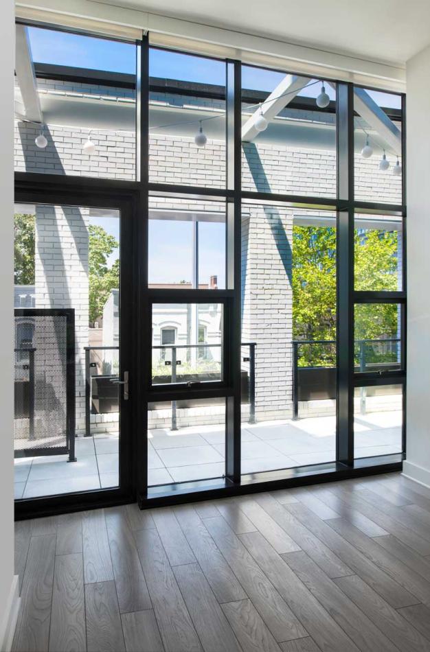 Bright, empty room with wood floors and large windows, situated in an apartment complex in Washington, D.C.