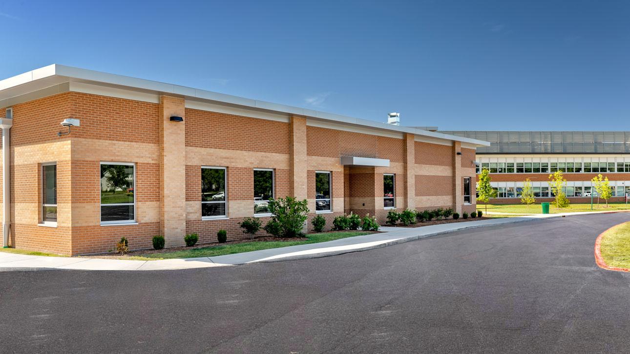 Winco supplied its FEMA 361 - ICC 500 window series, featuring a sturdy frame and impact-resistant laminated glass, for Kirkwood High School's storm shelter.  A substantial brick structure with a paved driveway, showcasing windows that meet strict storm shelter safety standards.