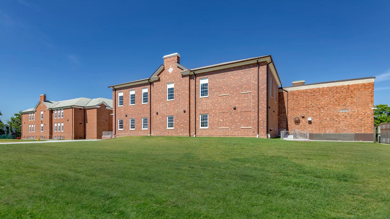 Both window series —1150S and FEMA 361 - ICC 500—provide Nipher Middle School with the historic look and storm shelter space administrators set out to achieve. Exterior brick building featuring historic replica windows with a grassy field in front and blue sky in the background.