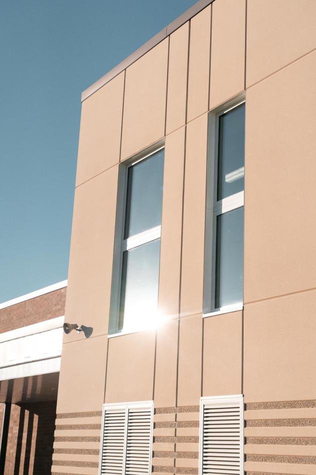 Rosemount Elementary School utilizes Winco’s 3250 window series and FEMA 361 – ICC 500 tornado-resistant windows used as Safe Rooms for storms. Close up of windows in a beige building facade and a door marked "4." It is surrounded by a neatly trimmed lawn and two young trees under a clear sky.
