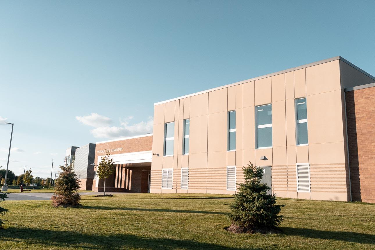 Rosemount Elementary School utilizes Winco’s 3250 window series and FEMA 361 – ICC 500 tornado-resistant windows used as Safe Rooms for storms. Modern school building with beige and brick facade under a clear blue sky. Manicured lawn and young trees create a peaceful, sunny atmosphere.