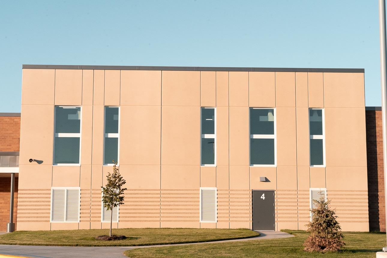 Rosemount Elementary School utilizes Winco’s 3250 window series and FEMA 361 – ICC 500 tornado-resistant windows used as Safe Rooms for storms. A beige building facade with vertical windows and a door marked "4." It is surrounded by a neatly trimmed lawn and two young trees under a clear sky.