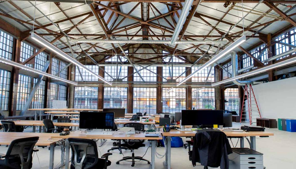 WINCO provided more than 48,000 square feet of its Series 3250 Steel Replica windows fitted with ¼” monolithic tempered clear glass. In addition to stunning aesthetics, the windows can withstand 110 mph winds as well as seismic activity. A large indoor room featuring a desk with chairs, with natural daylight illuminating the space.