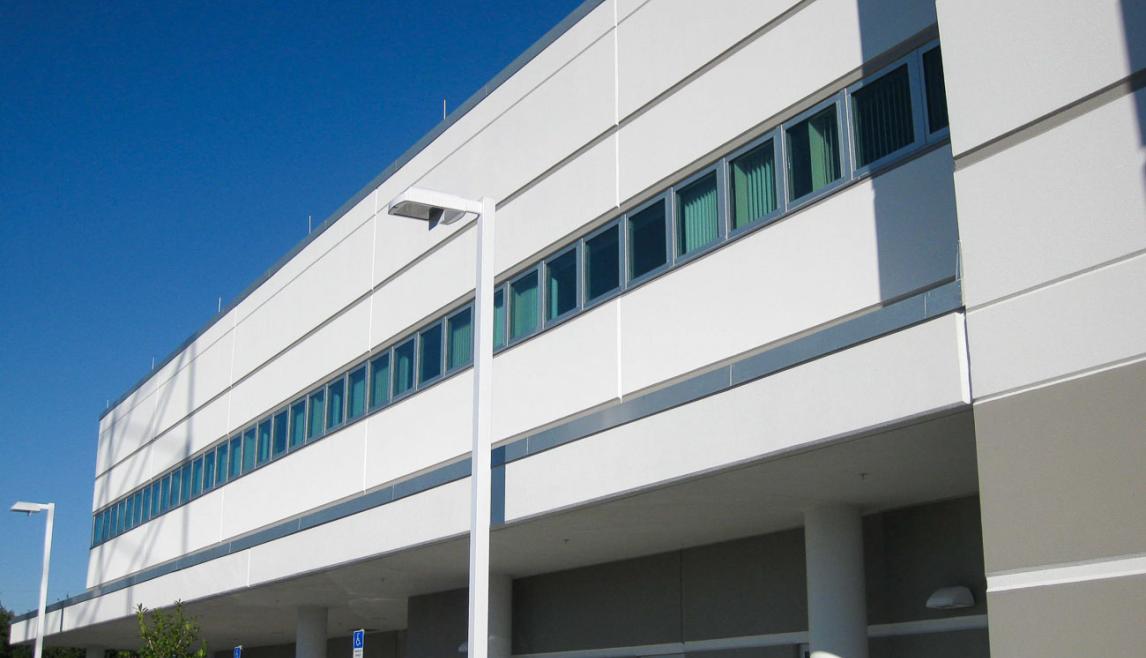 The Public Works Emergency Responders Building (PWERB) is a 2-story facility that is LEED Gold Certified and includes Winco tornado-rated windows. A tall commercial building with numerous windows against a clear blue sky. The architectural facade showcases a modern design, emphasizing the glass and structure of the property.
