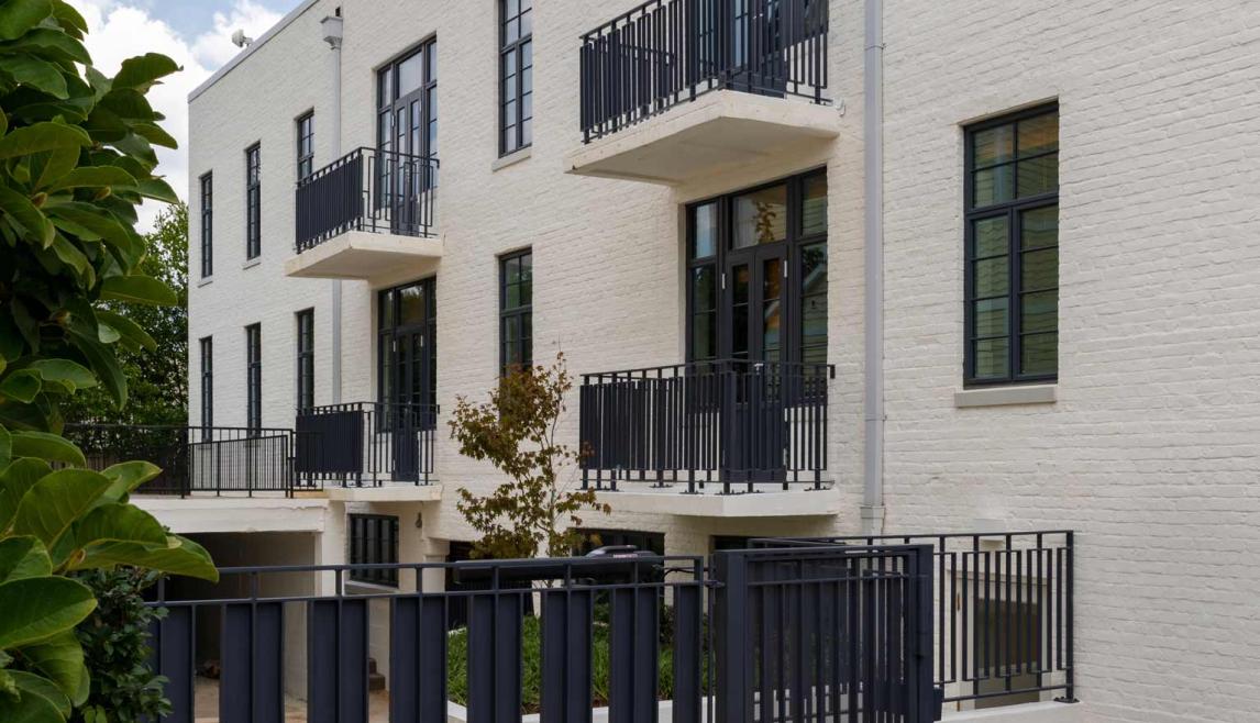 A white brick building featuring black metal gates and balconies, showcasing WINCO’s NC82 Terrace Doors for hurricane safety