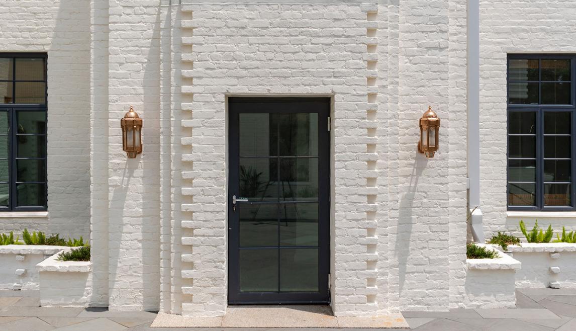 A white brick building featuring a large door, equipped with WINCO’s NC82 Terrace Doors for hurricane resistance.