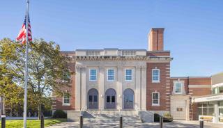 Exterior brick building featuring historic replica windows with a grassy field in front and blue sky in the background.