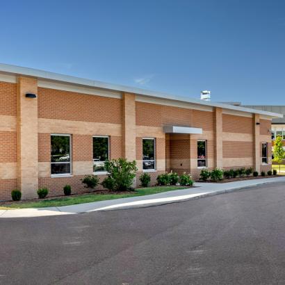 A substantial brick structure with a paved driveway, showcasing windows that meet strict storm shelter safety standards.